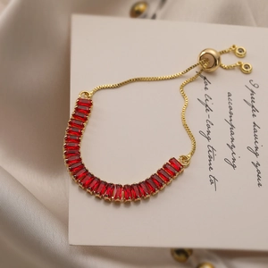 Detailed close-up of a gold-plated adjustable bracelet with baguette-cut red gemstones