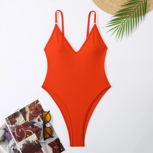 Flat lay of an orange deep V-neck one-piece swimsuit with beach accessories on white