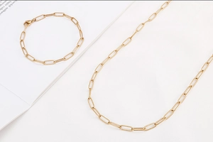 Close-up of gold paperclip chain necklace and bracelet set on a white book