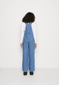 Rear view of loose dark blue denim overalls for women featuring back pockets and wide-leg design