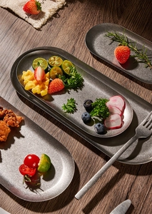 Macro view of oval stainless steel snack plates with food on a dark wood table
