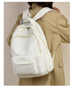 Rear view of model carrying a minimalist white nylon backpack with multi-zipper storage