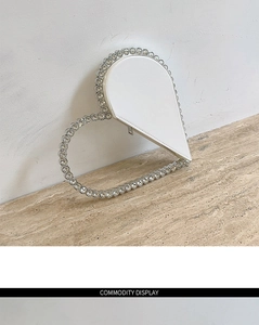 Macro shot of a white heart evening bag with crystal trim on a beige stone surface