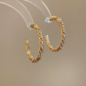 Close-up of golden twisted C-shaped earrings with intricate braided rope texture detail