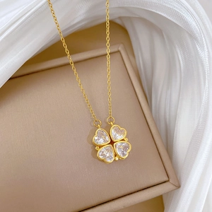 Close-up of golden four-leaf clover necklace with heart-shaped crystals on silk fabric