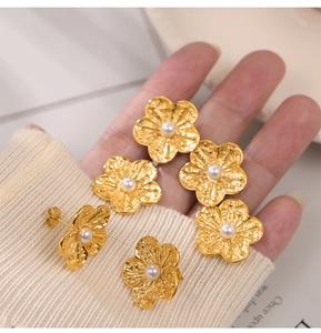 Close-up of gold flower stud earrings with wavy petals and white pearl centers