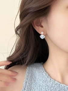 Detailed close-up of shell-shaped light blue earrings with pearl accents on model
