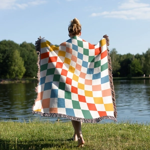 Detail of colorful bohemian checkered camping blanket with tassels shown in outdoor lake setting