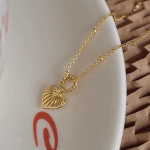 Macro shot of gold heart pendant necklace showing intricate radial texture and fine chain