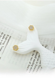 Close-up of hexagonal gold-plated titanium earrings with full white zircon inlay on a stand