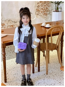 Little girl in grey pinafore dress styling a purple bow crossbody bag with gold chain