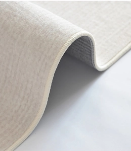 Close-up of beige short-pile rug showing fine edge stitching and anti-slip grey backing