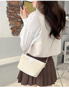Detail shot of a white crossbody bag with yellow dots and gold hardware on a model