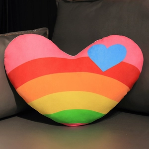 Rainbow striped heart-shaped plush pillow cushion on a modern grey sofa seat