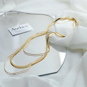 Close-up of triple-layered gold snake bone chain necklaces on a mirror surface