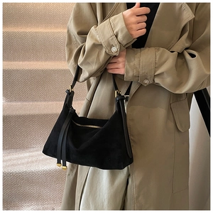 Detail of a black suede hobo bag featuring a gold zipper and long leather tassel charm