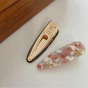 Close-up of ink-wash acrylic and gold-tone metal hair clips with engraved Korea lettering