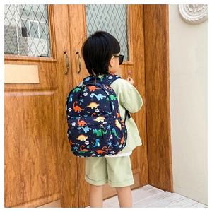 Rear view of a child wearing a navy blue dinosaur pattern backpack against a wood door