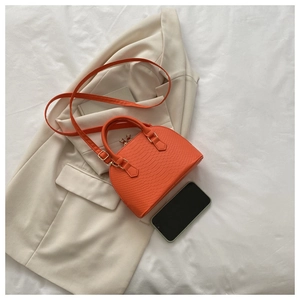Detailed macro view of orange crocodile texture handbag with smartphone for size reference