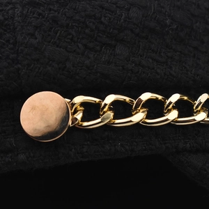 Detail of black tweed baker boy hat featuring a gold chain and round metallic button