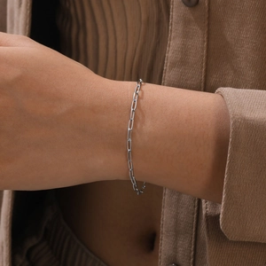 Close-up of polished silver paperclip chain bracelet on a model's wrist with knitwear