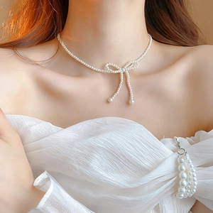 Detail of beaded pearl choker necklace with a woven bow design on a female model