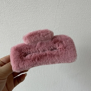 Detailed view of a soft pink faux fur hair claw clip held against a white textured wall