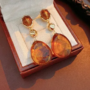 Vintage gold teardrop earrings with amber resin stones on textured brown leather