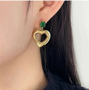 Close-up of gold hollow heart earrings with green square zircon stone worn by a model
