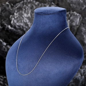 Macro shot of a delicate silver box chain necklace on a blue velvet jewelry stand