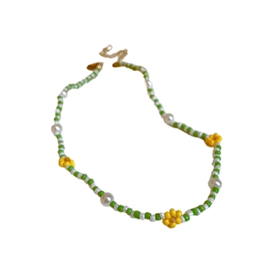 Beaded necklace with green seed beads, white pearls, and yellow flower accents on white back