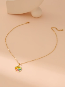 Detail view of a gold chain necklace with a colorful lemon slice pendant on beige backdrop