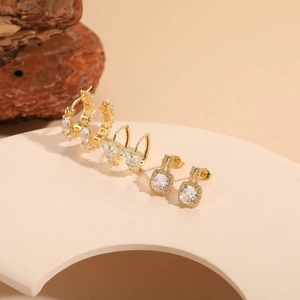 Close-up of gold zircon earrings set featuring butterfly hoop and square stud designs