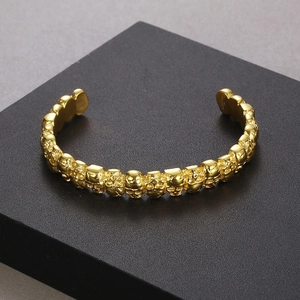 Detailed close-up of gold skull cuff bracelet with gothic punk design on dark stand