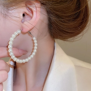 Close-up of elegant large white pearl hoop earrings worn by a model in soft lighting