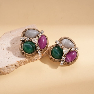 Detail of vintage gold earrings featuring green, purple, and grey cabochon stones and crystals