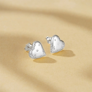 Detailed close-up of heart-shaped silver stud earrings with sparkling white crystals