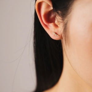 Detailed close-up of a curved gold feather stud earring featuring pavé-set clear zircons