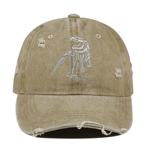 Close-up of khaki distressed baseball cap featuring white dinosaur skeleton embroidery