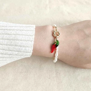 Close-up of pearl bracelet with gold clasp and a red chili pendant on woman's wrist