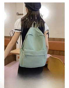 Detailed back view of a minimalist light green large capacity backpack worn by a model