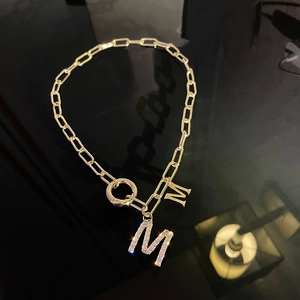 Détail de la chaîne trombone dorée avec doubles pendentifs lettre M et strass brillants