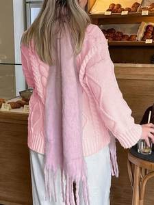Pink chunky knit cardigan with light purple fringe scarf viewed from the back in a cafe