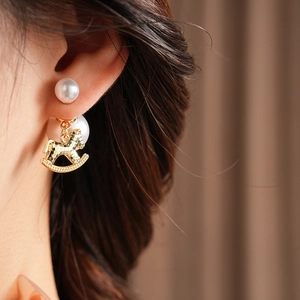 Close-up of golden rocking horse earring with pearl stud worn on model's ear