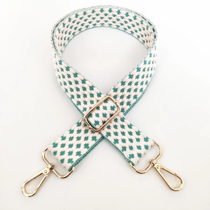 Detail of adjustable woven purse strap with teal cross pattern and gold metal hardware