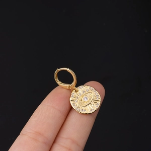 Close-up of golden Evil Eye pendant earring with textured rays and clear crystals