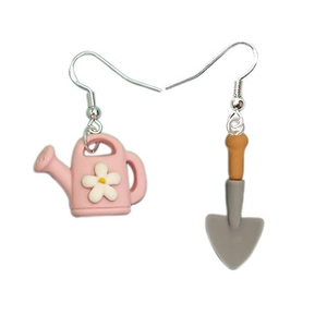 Detail view of cute asymmetrical gardening earrings with pink watering can and small shovel