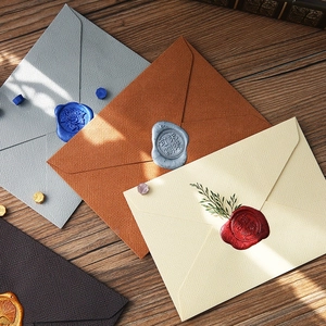 Vintage textured linen paper envelopes with wax seal and dried flowers on wooden desk