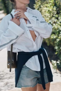 Detail of white loose shirt featuring contrast black sleeve stripes for sporty casual style