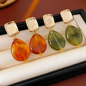 Detail of vintage square gold stud earrings with orange and green resin teardrop pendants